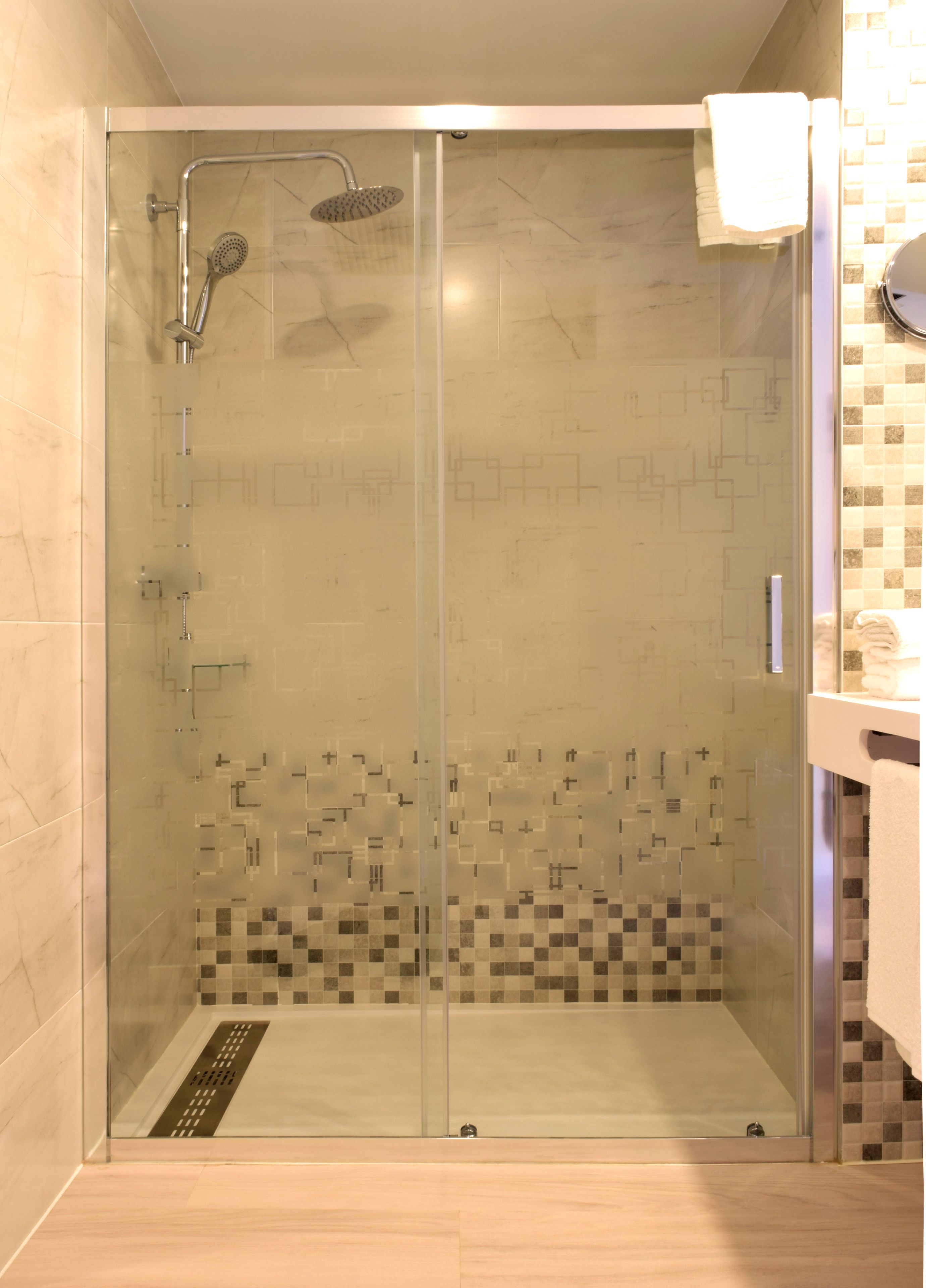 Une douche fermée par des parois en verre, avec un sol carrelé et une douchette à main.