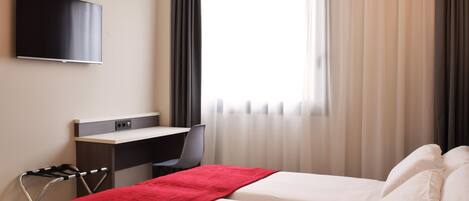 Habitación de hotel con cama, escritorio, silla y televisor montado en la pared.