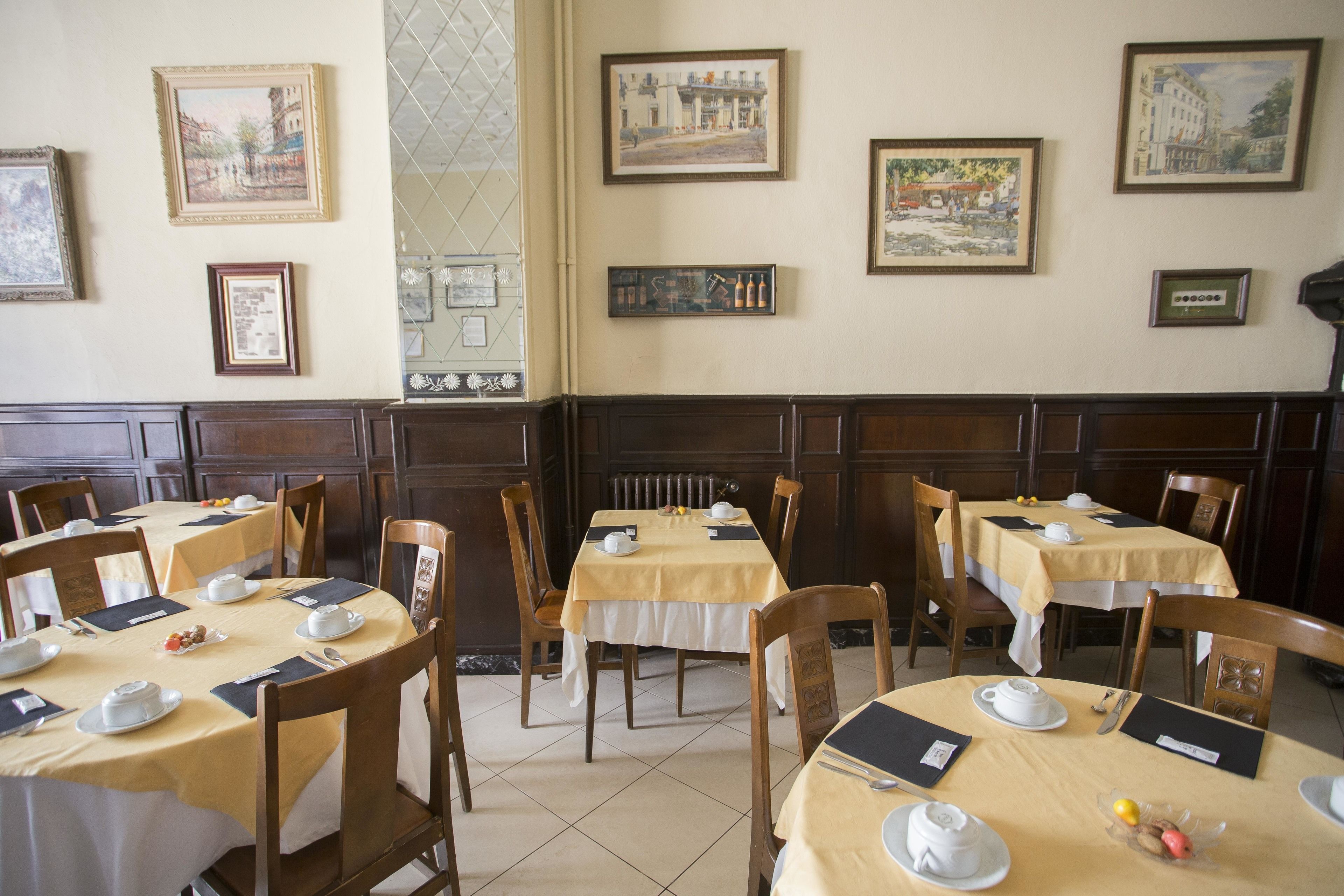Un comedor con mesas dispuestas para el desayuno, cuadros en las paredes y sillas de madera.