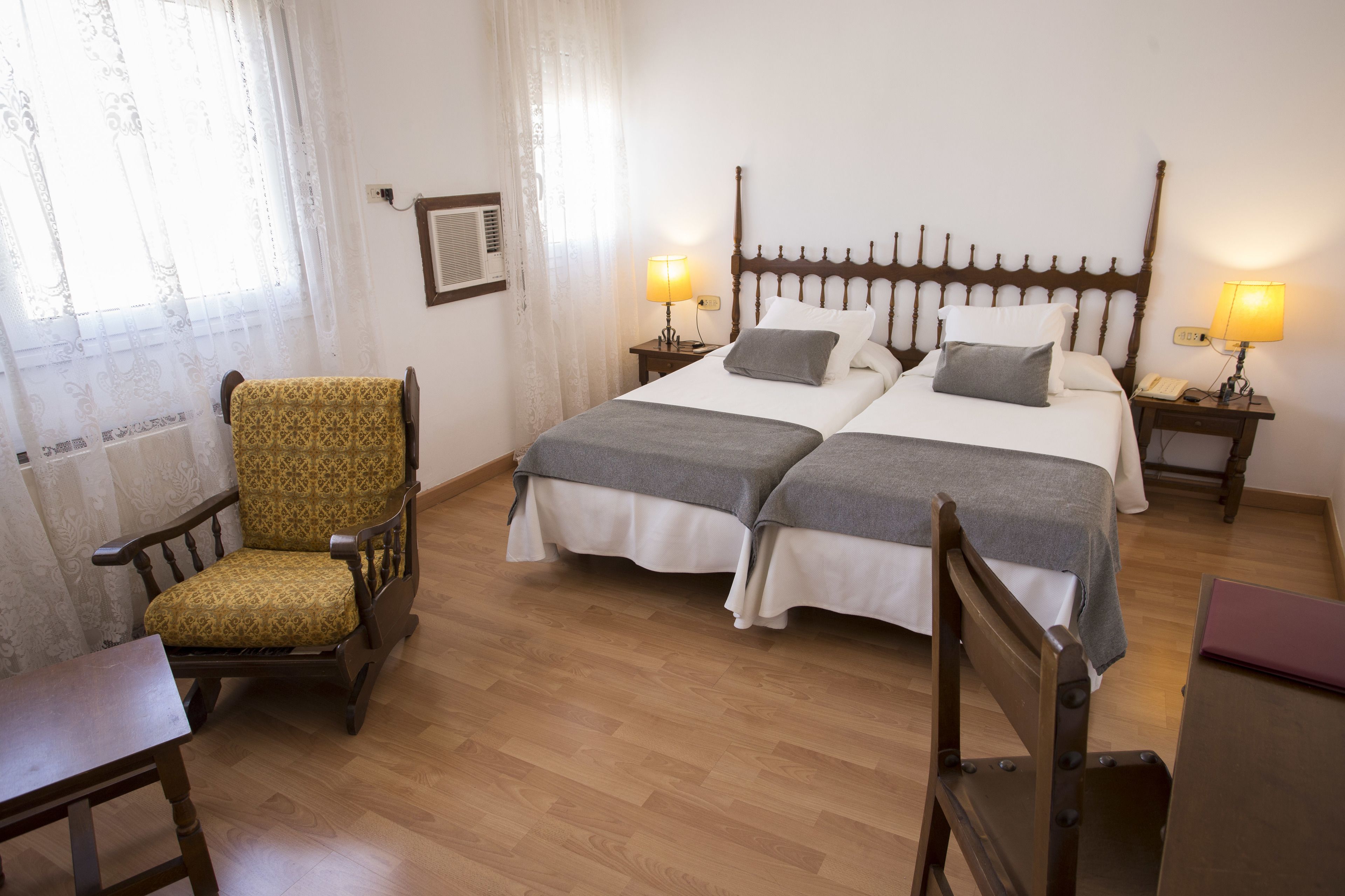 Une chambre double avec deux lits, une chaise en bois, une petite table et deux lampes de chevet.