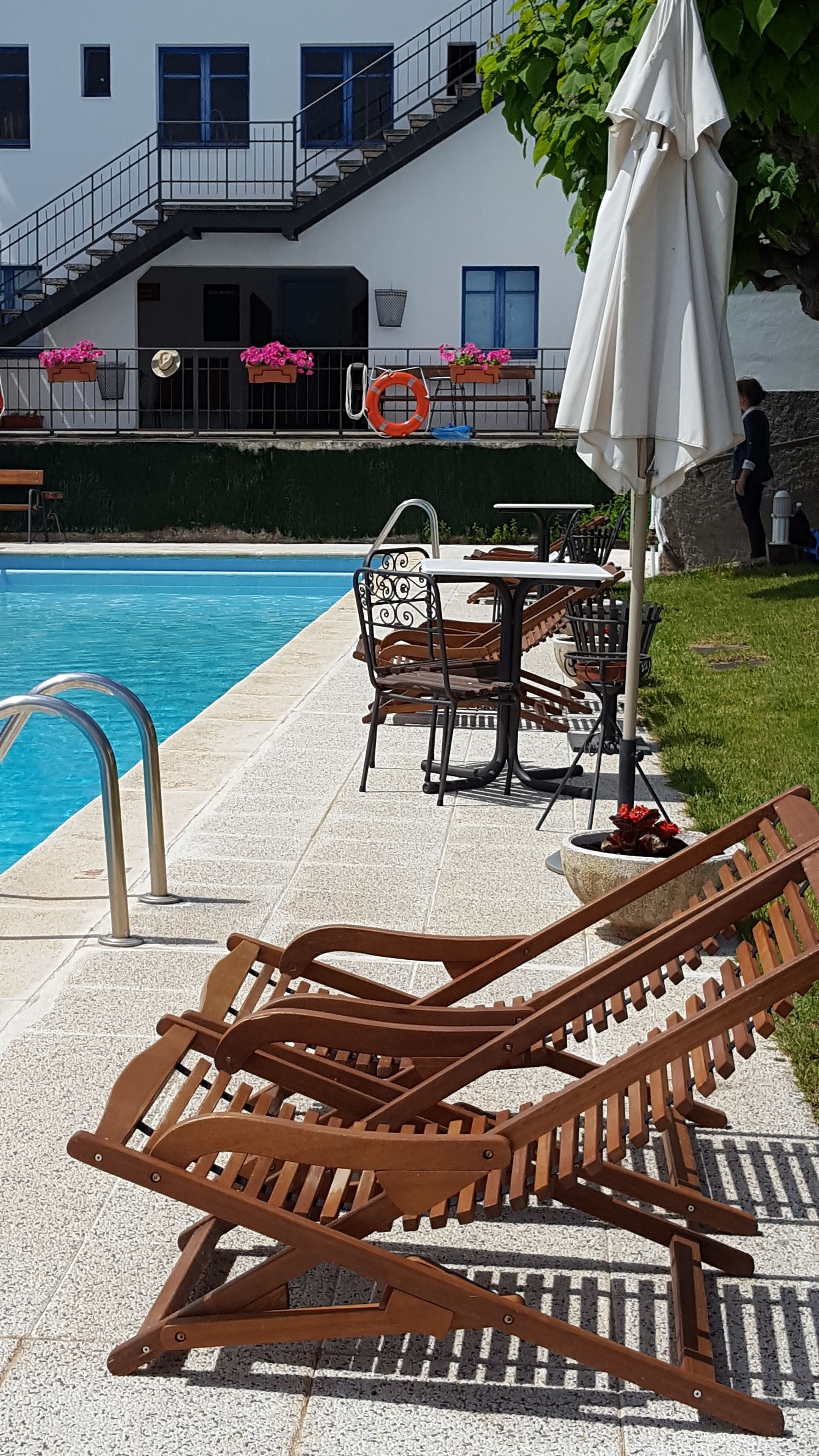 A poolside area with wooden lounge chairs, a table, and an umbrella.