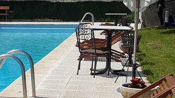 Un área junto a la piscina con sillones de madera, una mesa y una sombrilla.