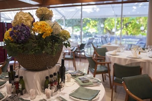 A dining area with tables set for a meal, a centerpiece of flowers, and various bottles and glasses on the tables.