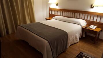 Quarto de hotel com cama, mesa de cabeceira com telefone e luminária na parede.