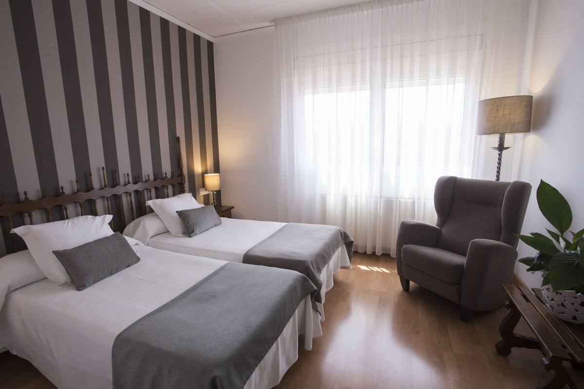 A hotel room with two beds, a chair, a lamp, and a potted plant.