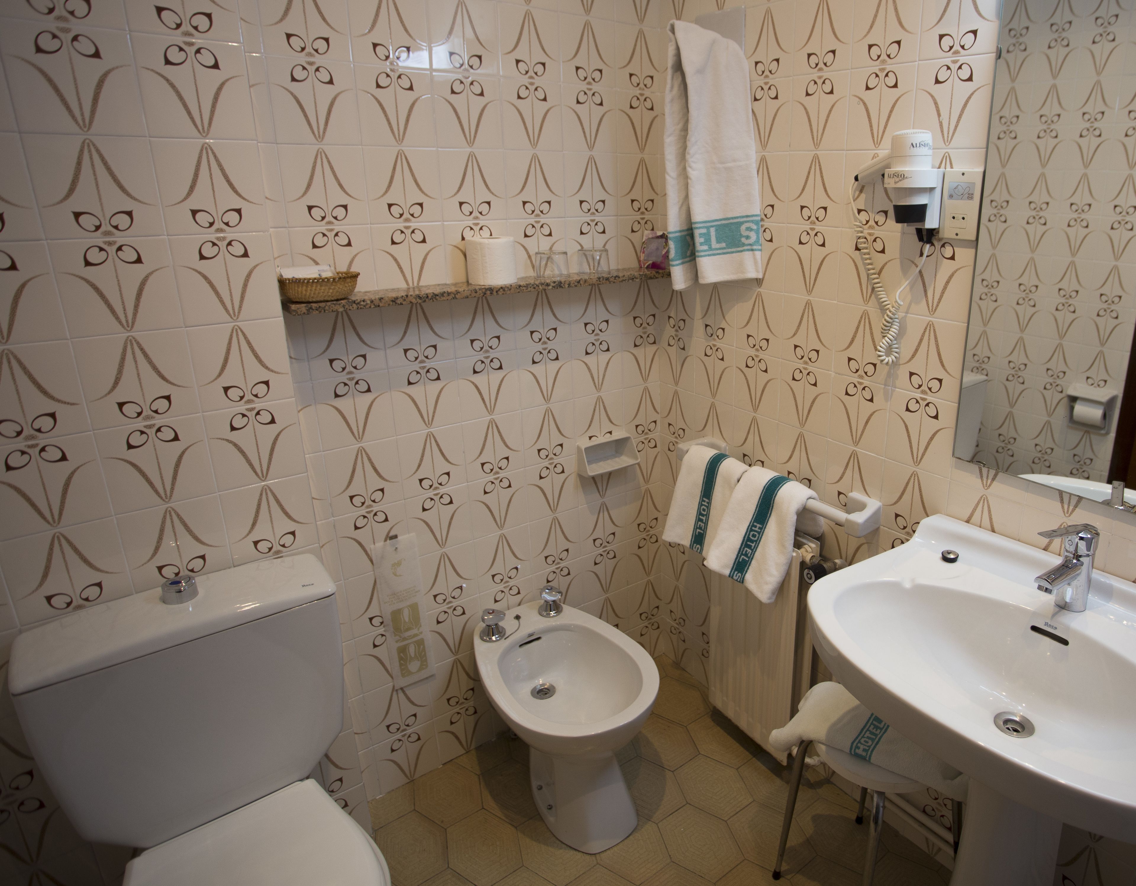 Ein Badezimmer mit Toilette, Bidet und Waschbecken, alles mit einem floralen Fliesendesign an den Wänden.
