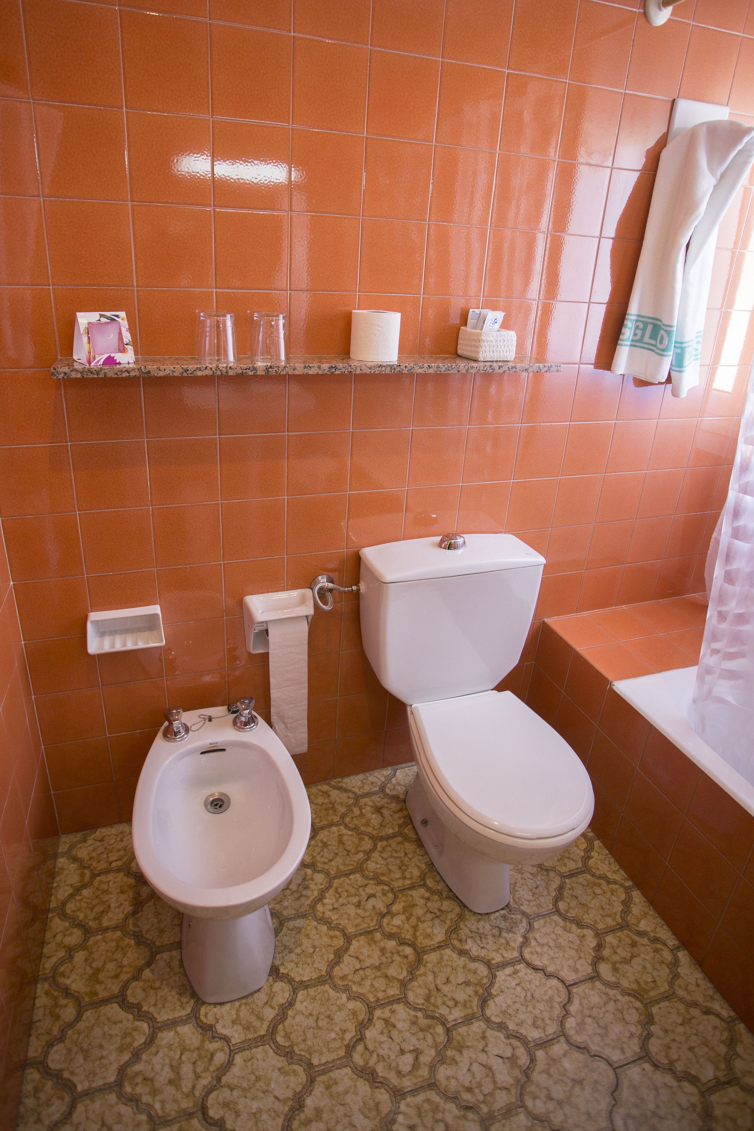 A bathroom with a bidet, toilet, and a shelf with toiletries.