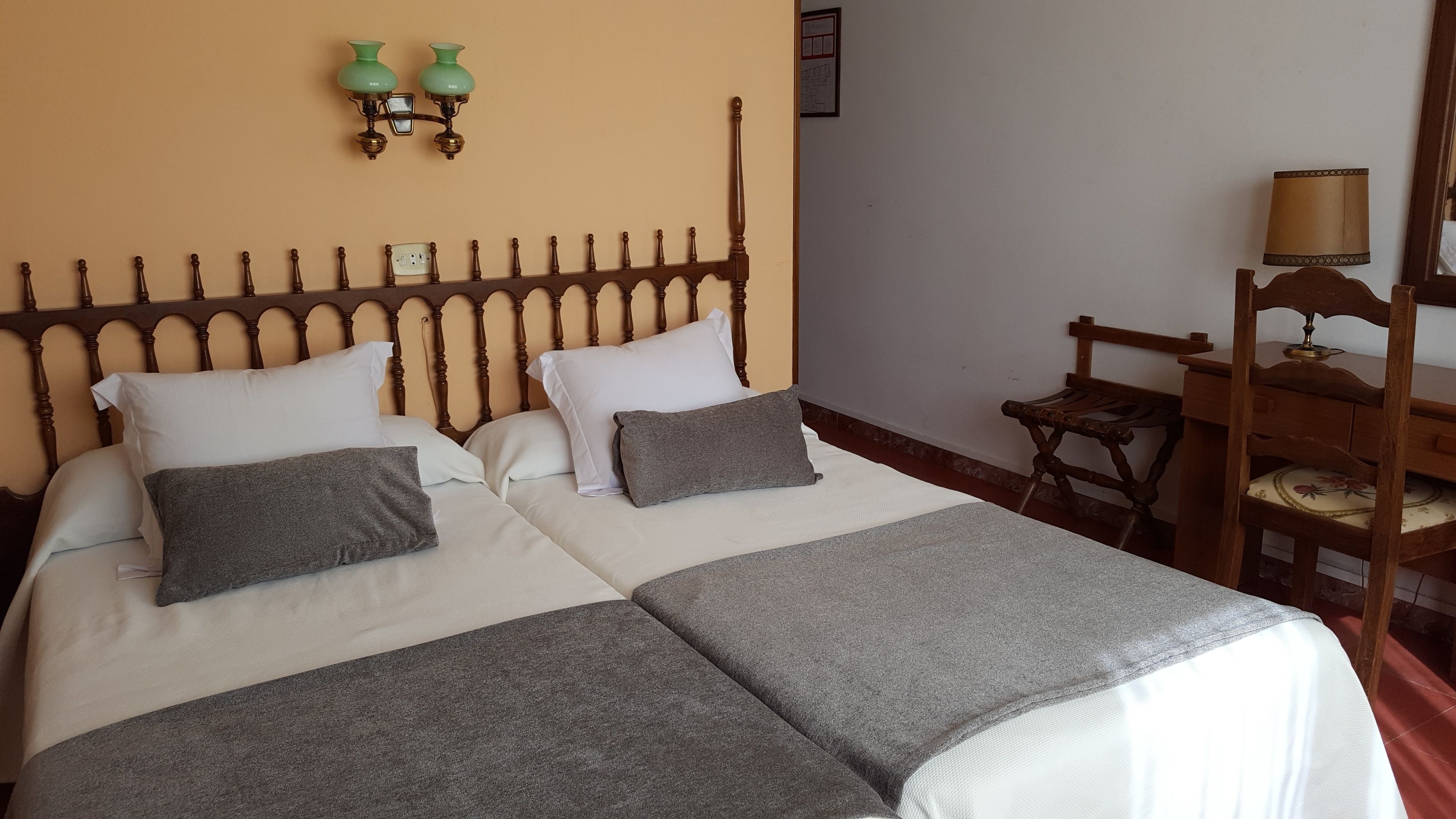 Cama doble con cabecera de madera, dos almohadas blancas y dos cojines grises.