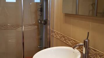 A bathroom with a glass shower enclosure, a white sink with a wooden countertop, and a mirror above the sink.