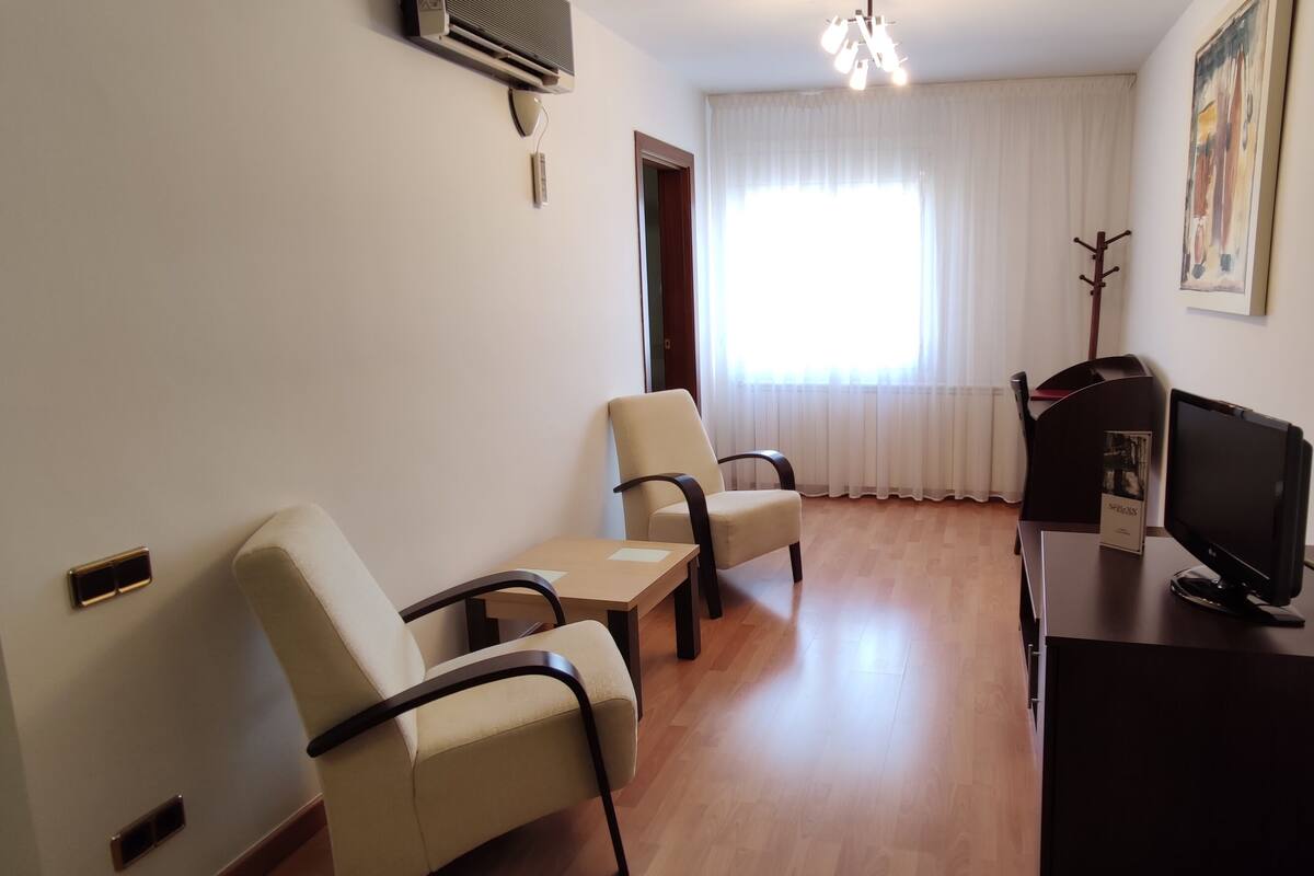 A room with a desk, two chairs, a television, and a coat rack.