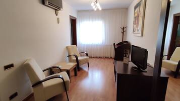 A room with a desk, two chairs, a television, and a coat rack.