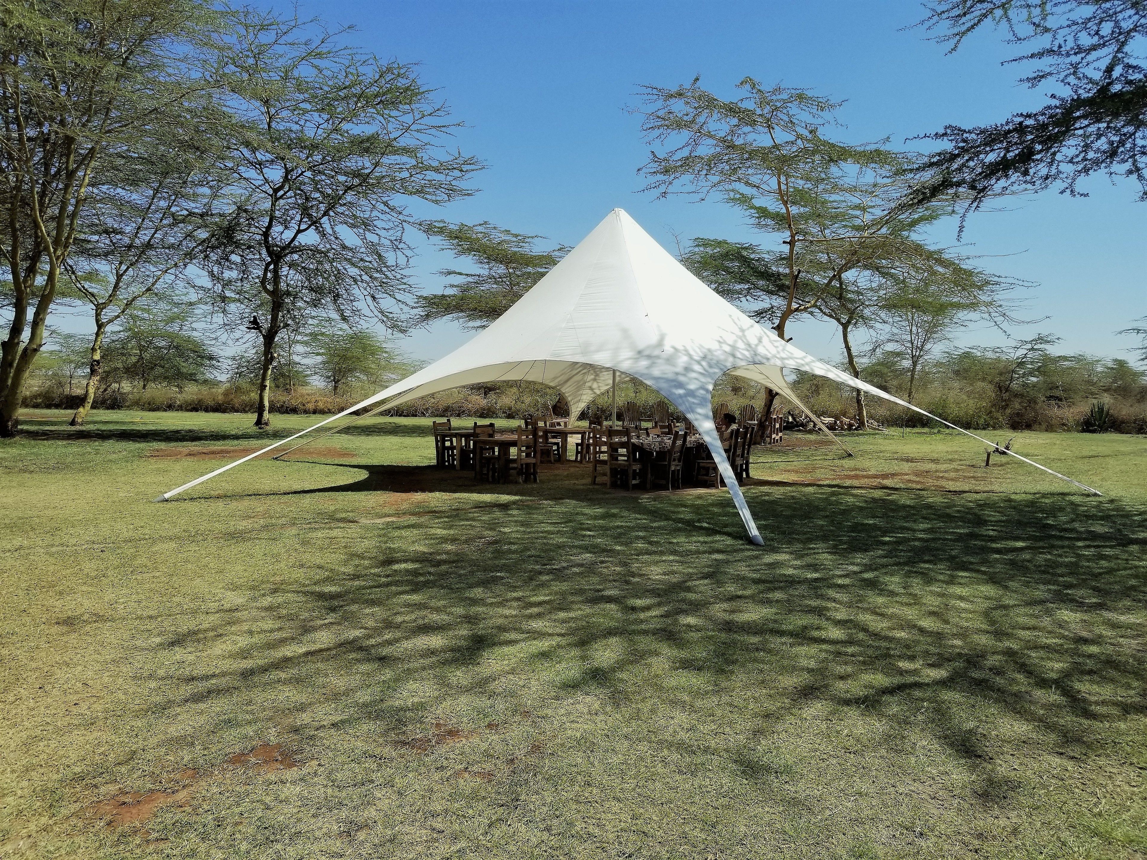 A white tent with a conical roof structure set up on a grassy field with trees in the background.