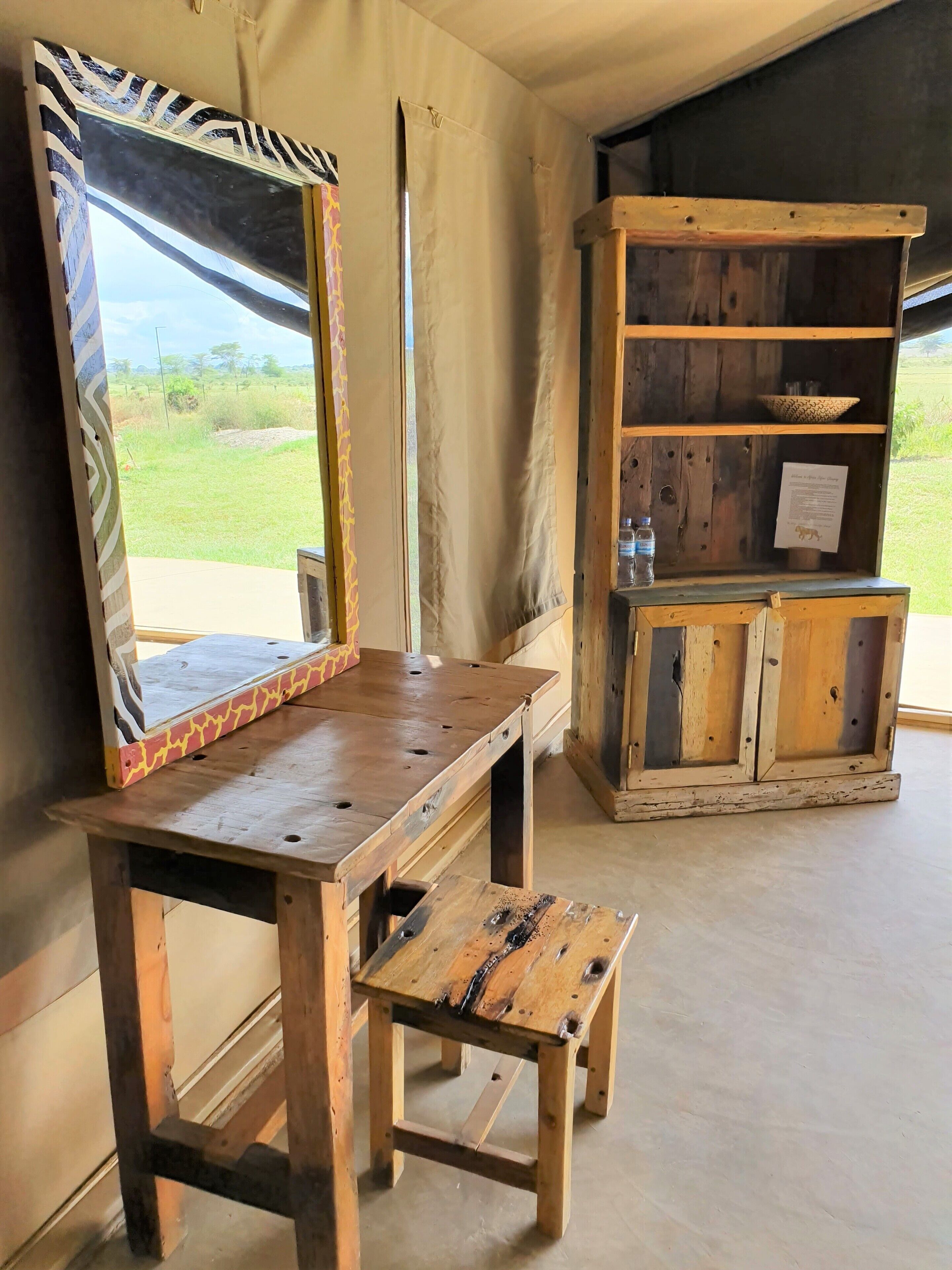 A wooden table with a mirror and a shelf unit with a water bottle and a sign.