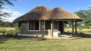 Ein Haus mit einem Strohdach und einer kleinen Veranda, umgeben von Gras und Bäumen.