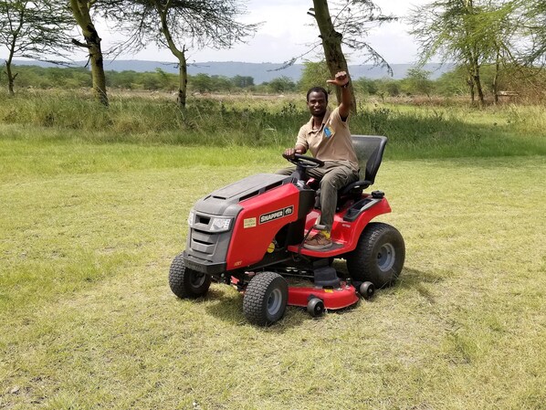 A person operating a red Snapper lawn tractor in a grassy field with trees and distant mountains in the background.