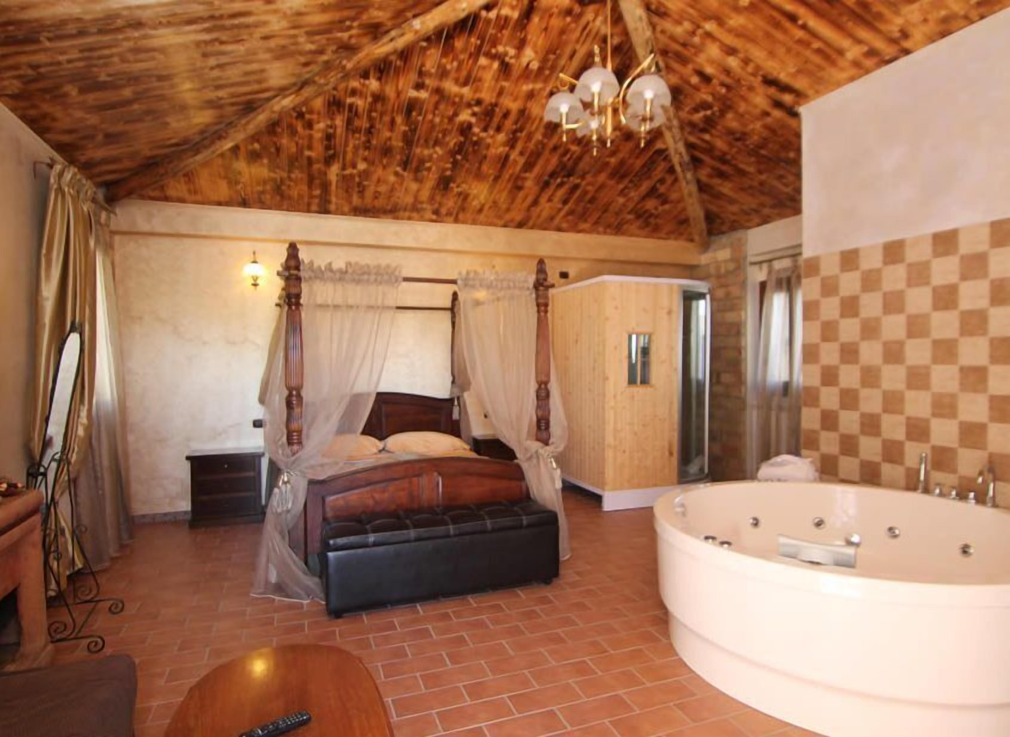A bedroom with a four-poster bed, a large bathtub, and a wooden ceiling.