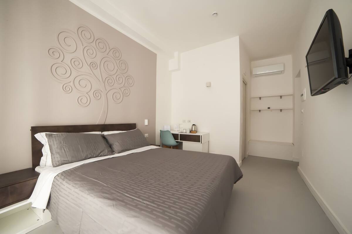 A modern bedroom with a large bed, a desk, a chair, and a mounted TV.