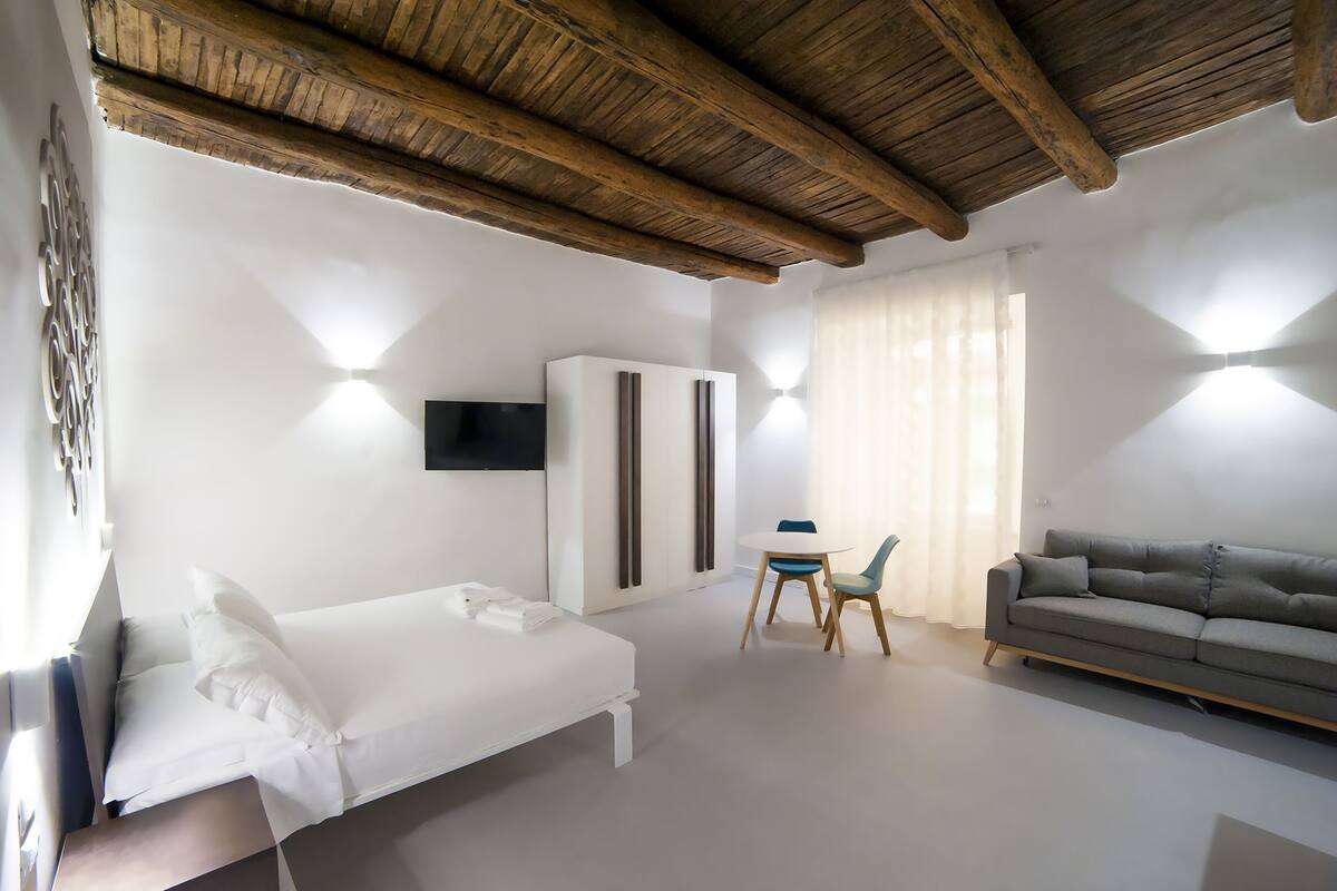 A modern bedroom with a wooden ceiling, a bed, a sofa, a TV, and a desk with a chair.