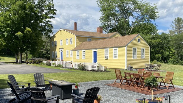 A yellow house with a white picket fence, outdoor seating with chairs and a table, and a gravel patio. - Colonel Spencer Inn (Campton)