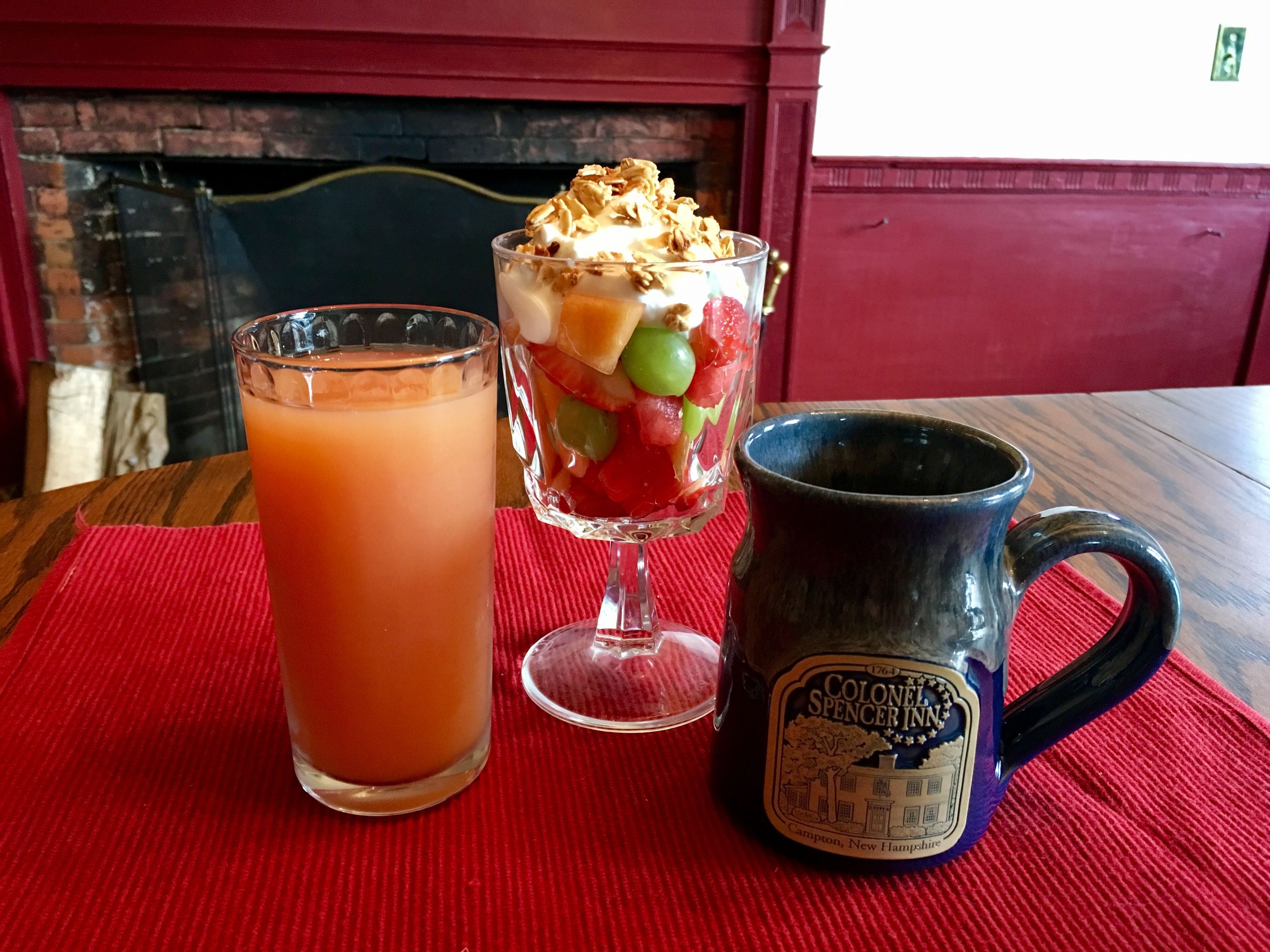 A table with a glass of iced tea, a layered dessert in a glass, and a mug with a label.