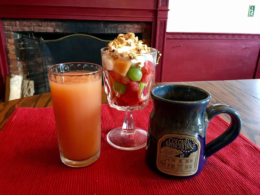 A table with a glass of iced tea, a layered dessert in a glass, and a mug with a label.