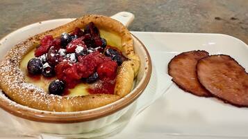 A dessert dish with berries and powdered sugar, and two slices of ham on a white plate.