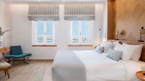 A modern hotel room with a large bed, two windows with view, a chair, and a desk. - Avra Apartments Venetian Harbour (Chania)