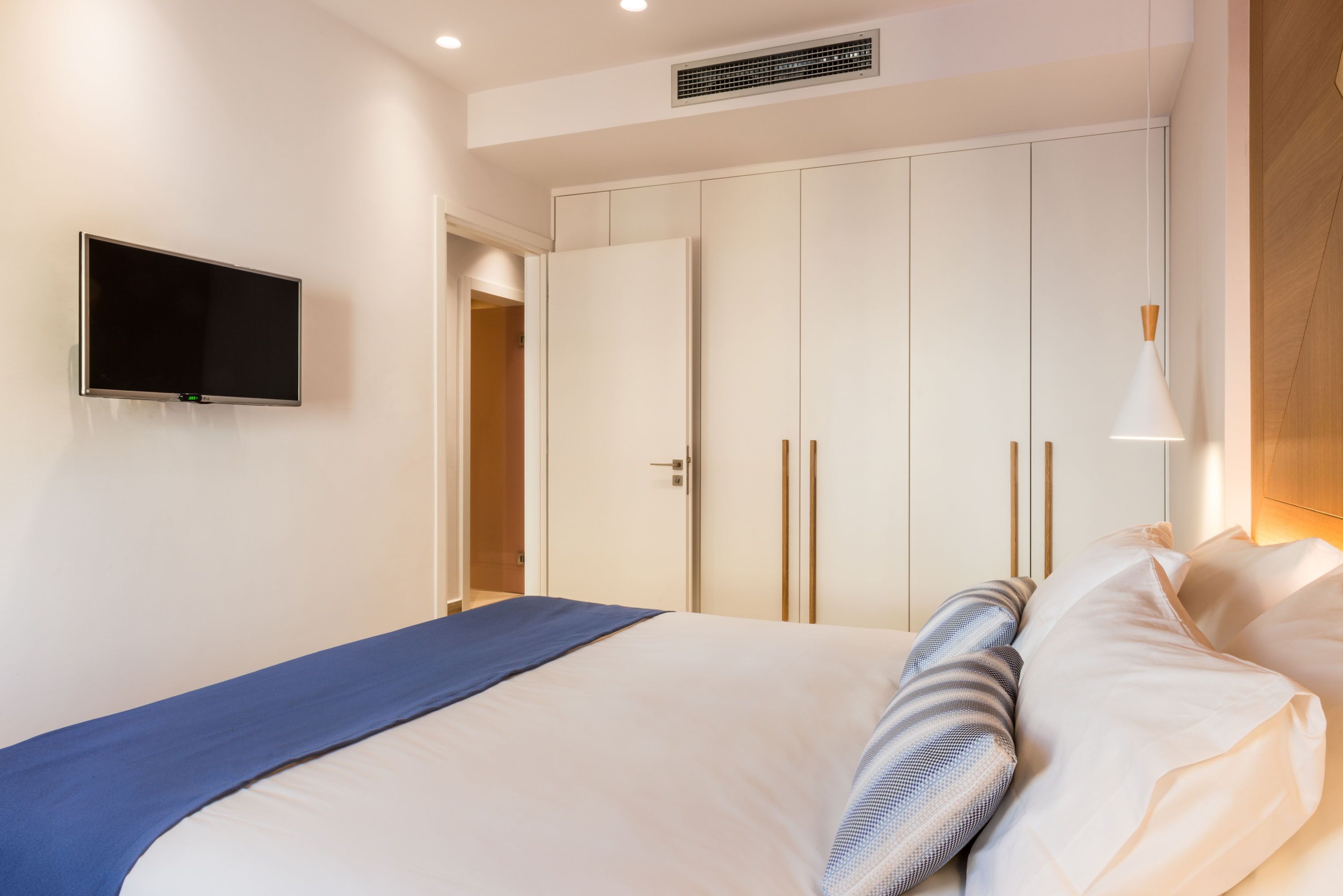 Un dormitorio con una cama, un televisor montado en la pared y un armario con puertas correderas.