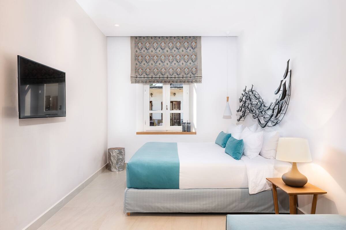 Una camera da letto moderna con un letto, un comodino, una lampada, un'opera d'arte e una TV a parete.