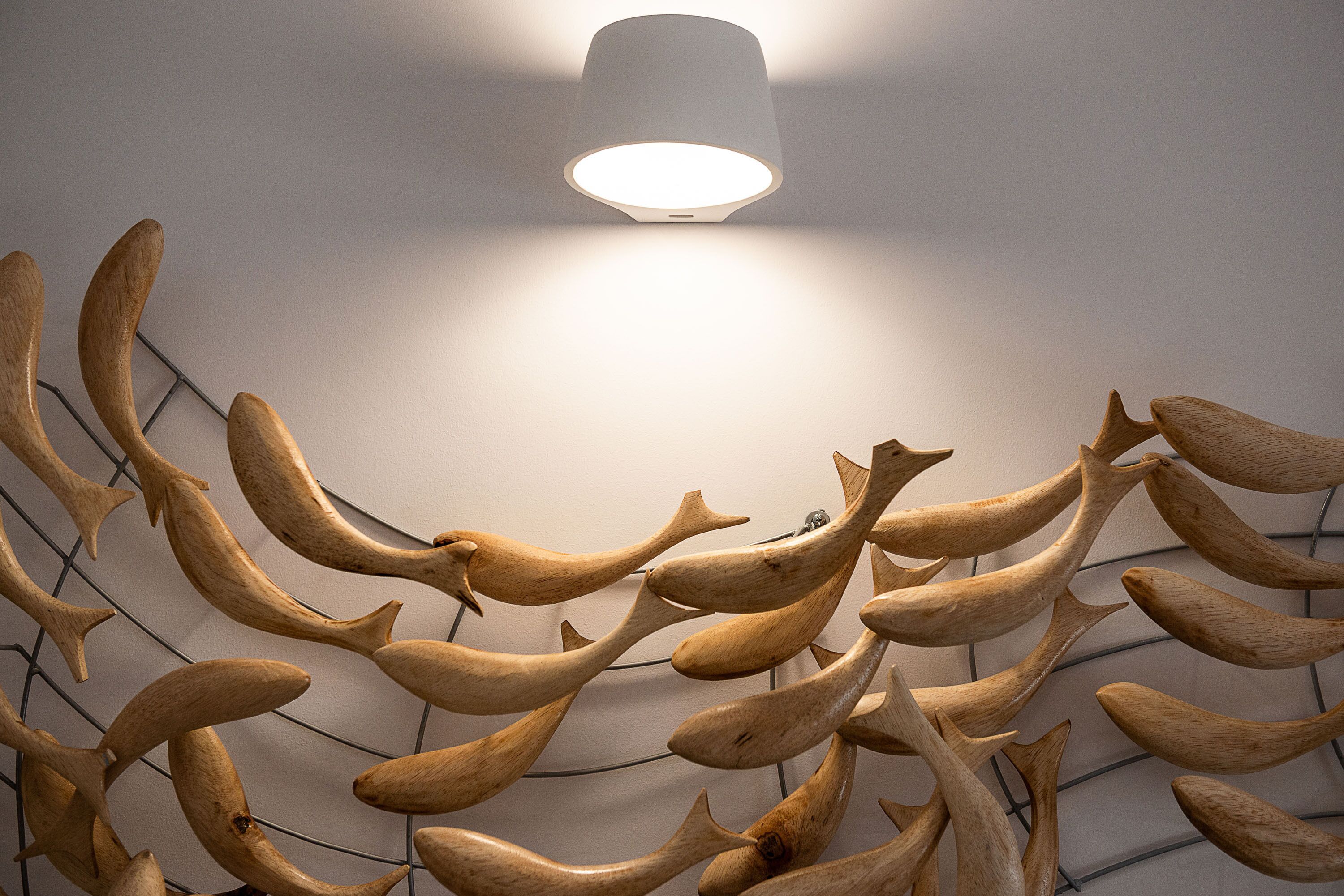Techo con una lámpara moderna y una pared con una escultura de pez de madera única.
