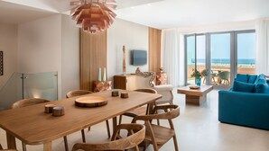 A modern living room with a wooden dining table, blue sofa, and large windows overlooking the beach. - Avra Apartments Venetian Harbour (Chania)