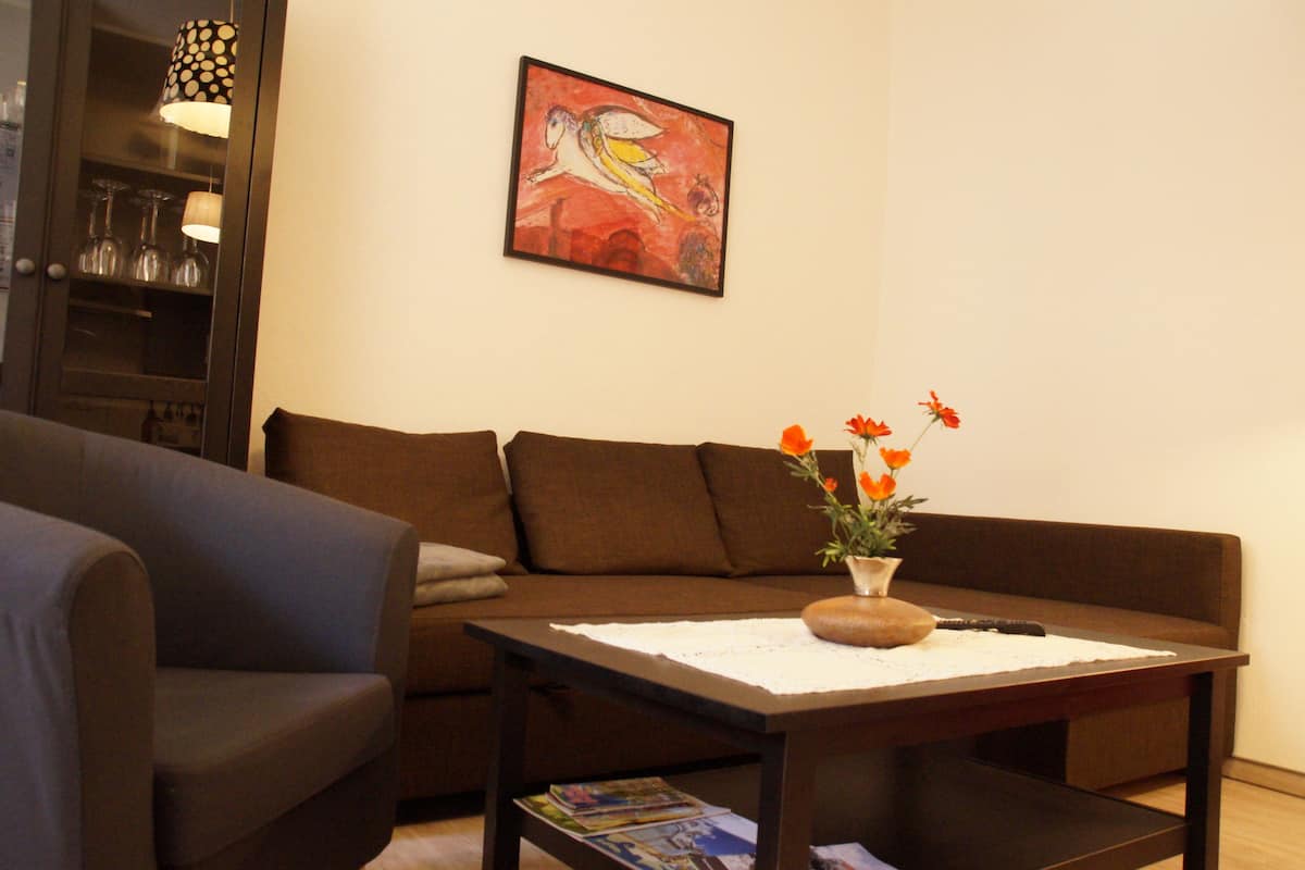 A living room with a brown sofa, a coffee table with a vase of flowers, and a painting on the wall.