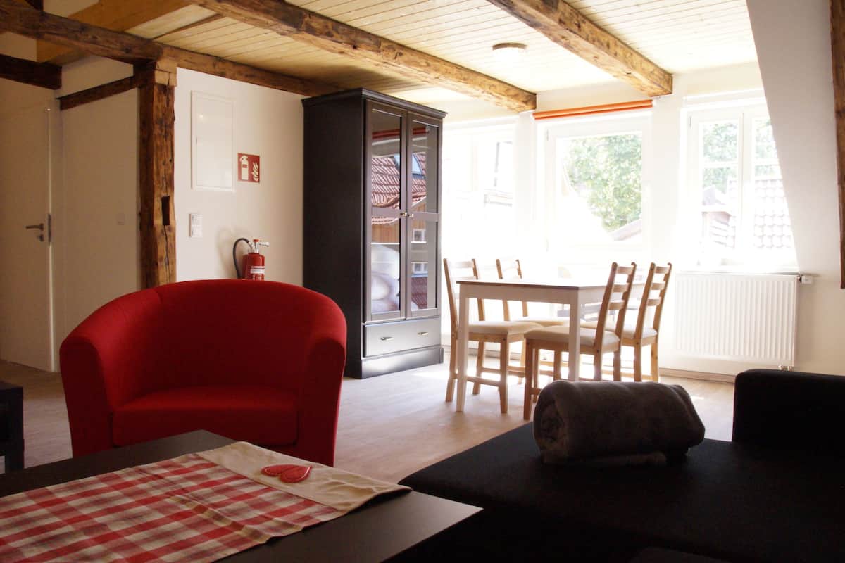 A living room with a red armchair, a black sofa, a dining table with chairs, and a black cabinet.