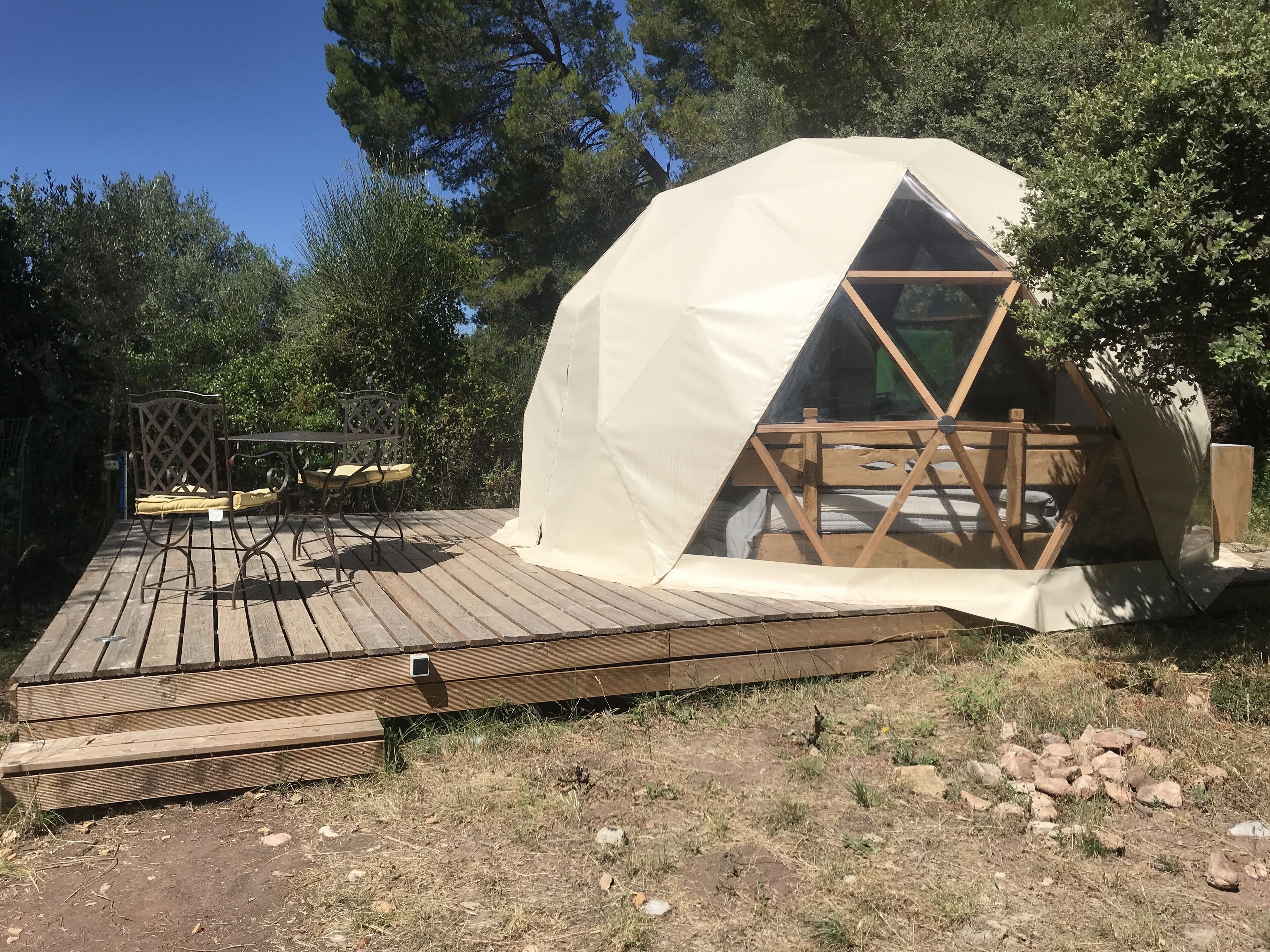 Una tenda a forma di cupola con un pontile in legno e un tavolo in metallo con sedie.