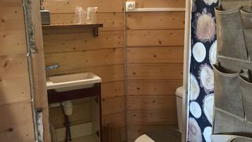 Un baño pequeño de madera con inodoro, lavamanos y zona de ducha.