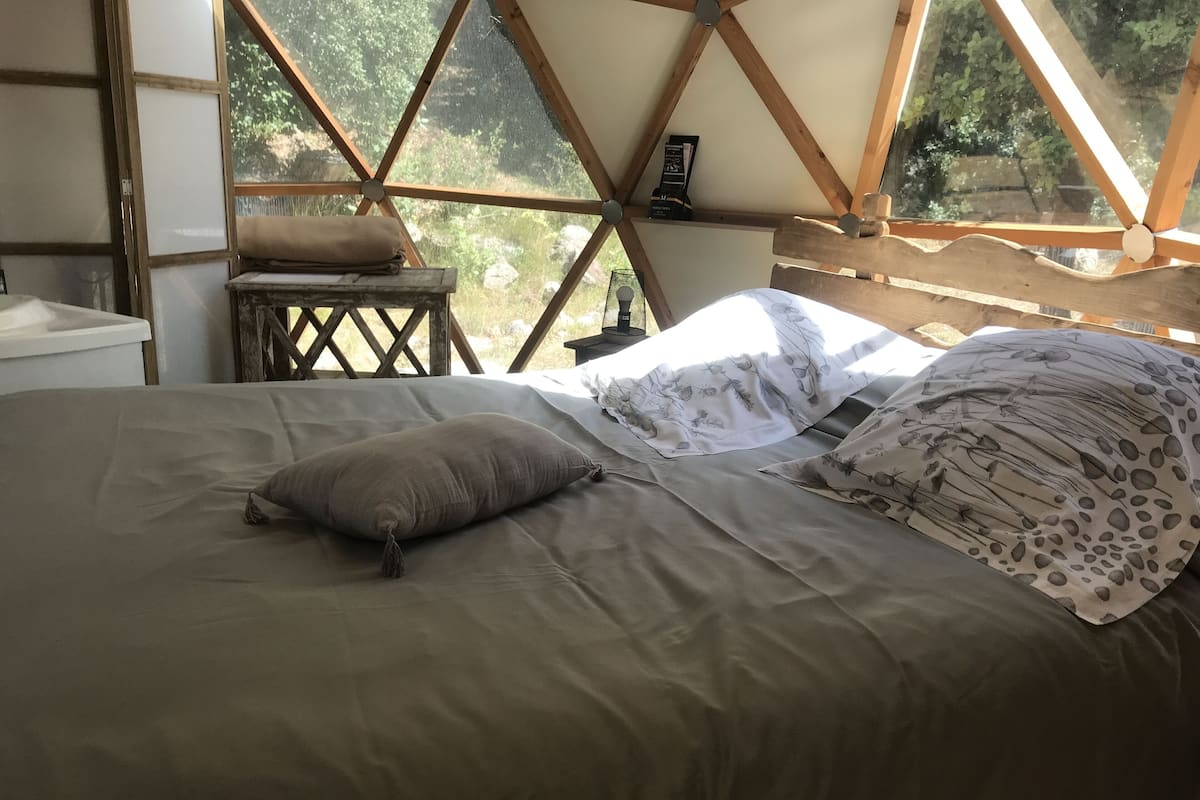 Un dormitorio acogedor con cama, almohadas y un pequeño taburete de madera.