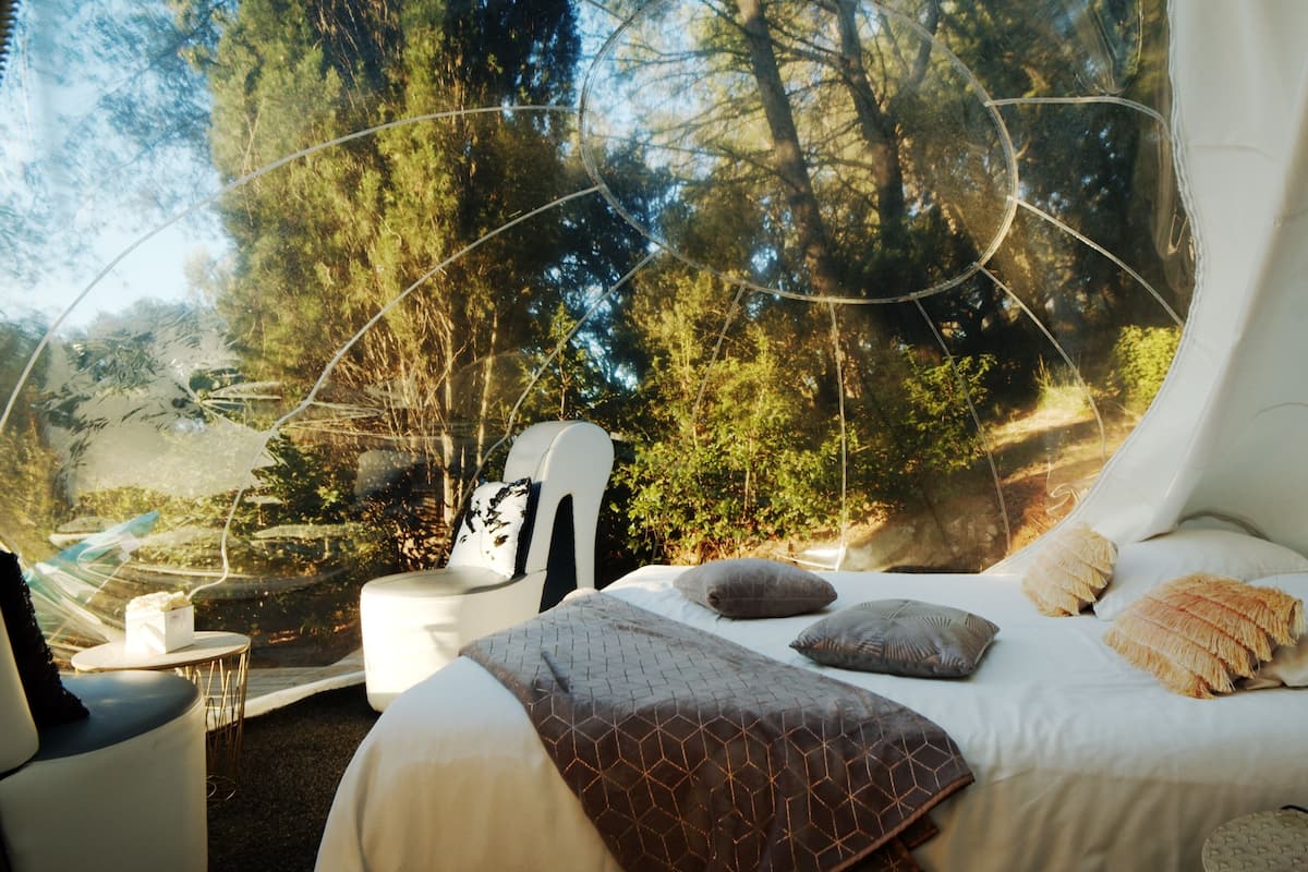 Un dormitorio acogedor con cama, almohadas y vistas a un bosque a través de un ventanal grande.