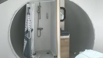 Una ventana circular con zona de ducha, un mueble de madera y un espejo.