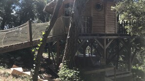 Une cabane dans les arbres avec une terrasse en bois et un pont de corde.