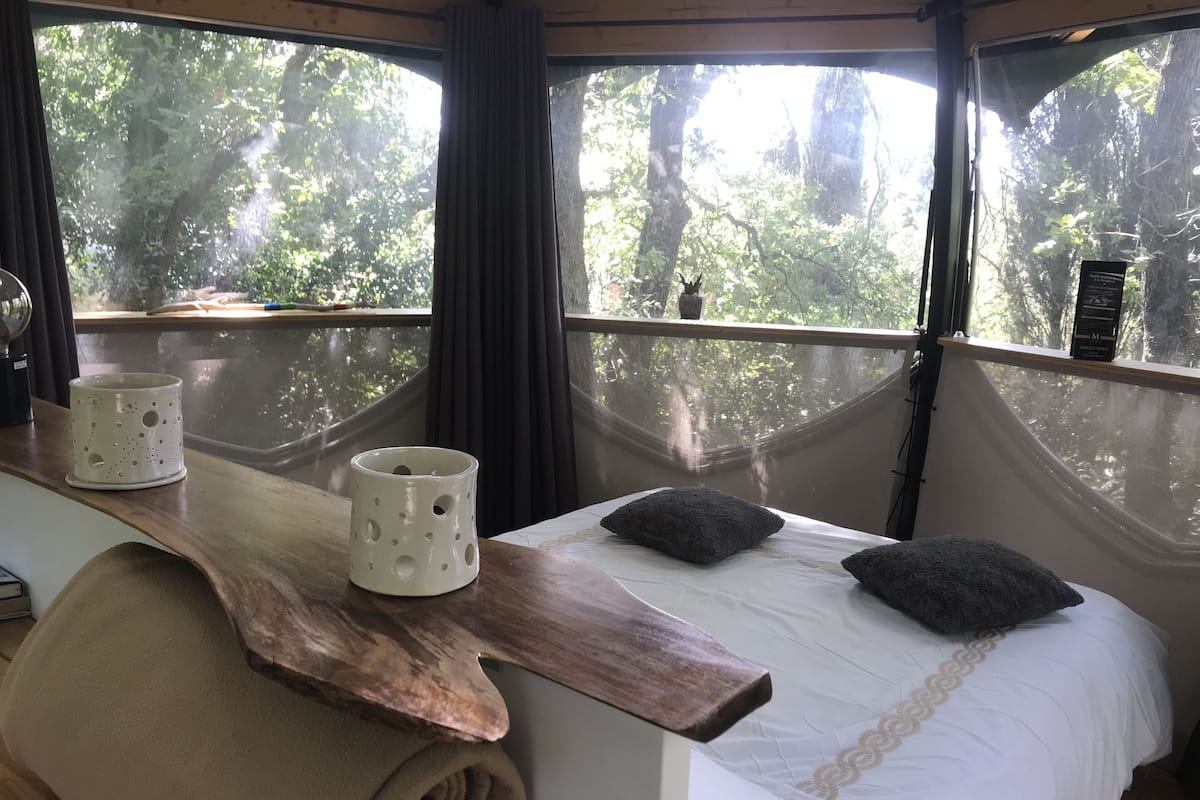 Una cama con cabecera de madera, dos almohadas y una taza blanca sobre una mesa de madera.
