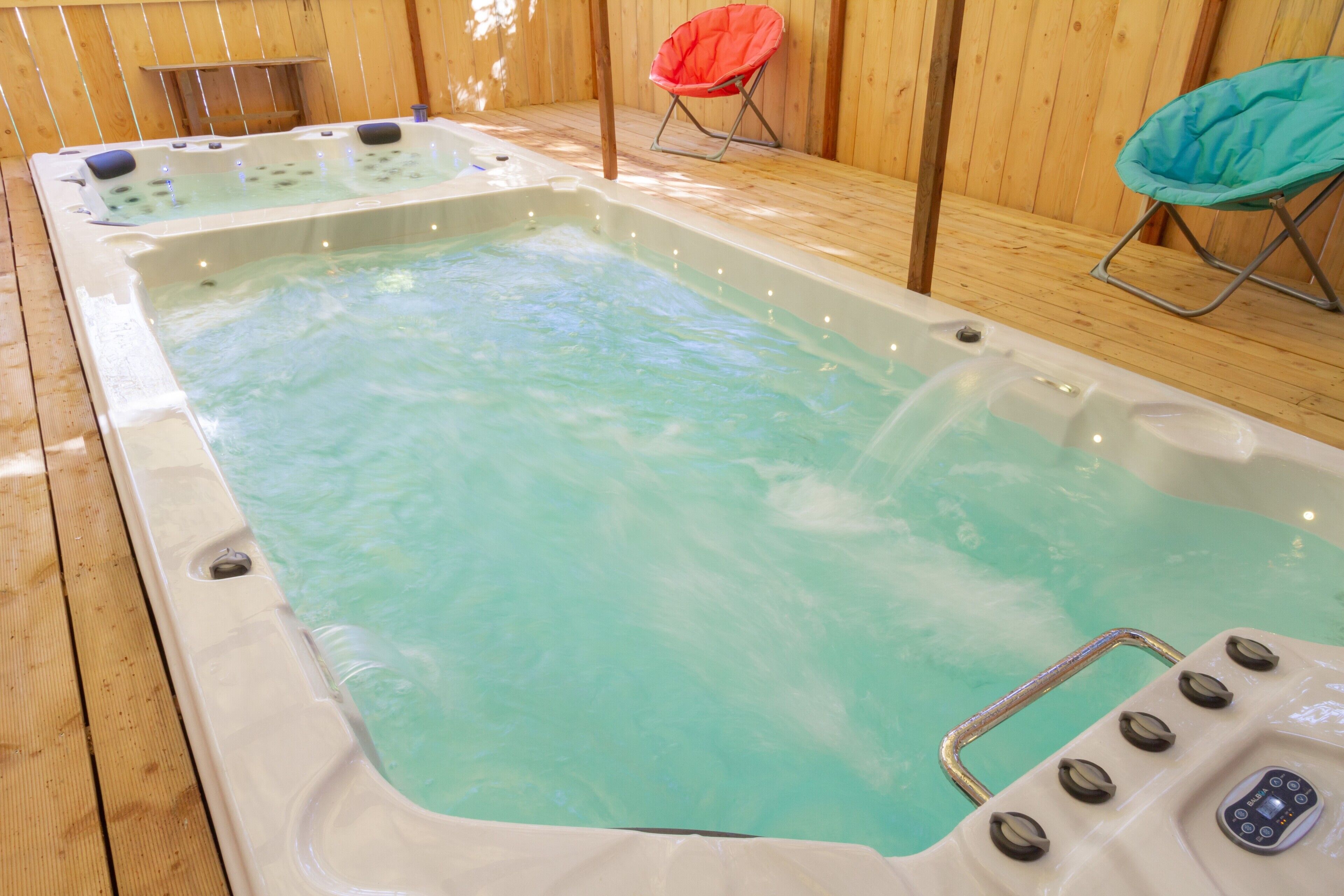 Un jacuzzi con controles, rodeado de piso de madera y dos sillas.