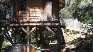 Une cabane en bois perchée dans un arbre, avec une échelle de corde, un jacuzzi et un hamac.