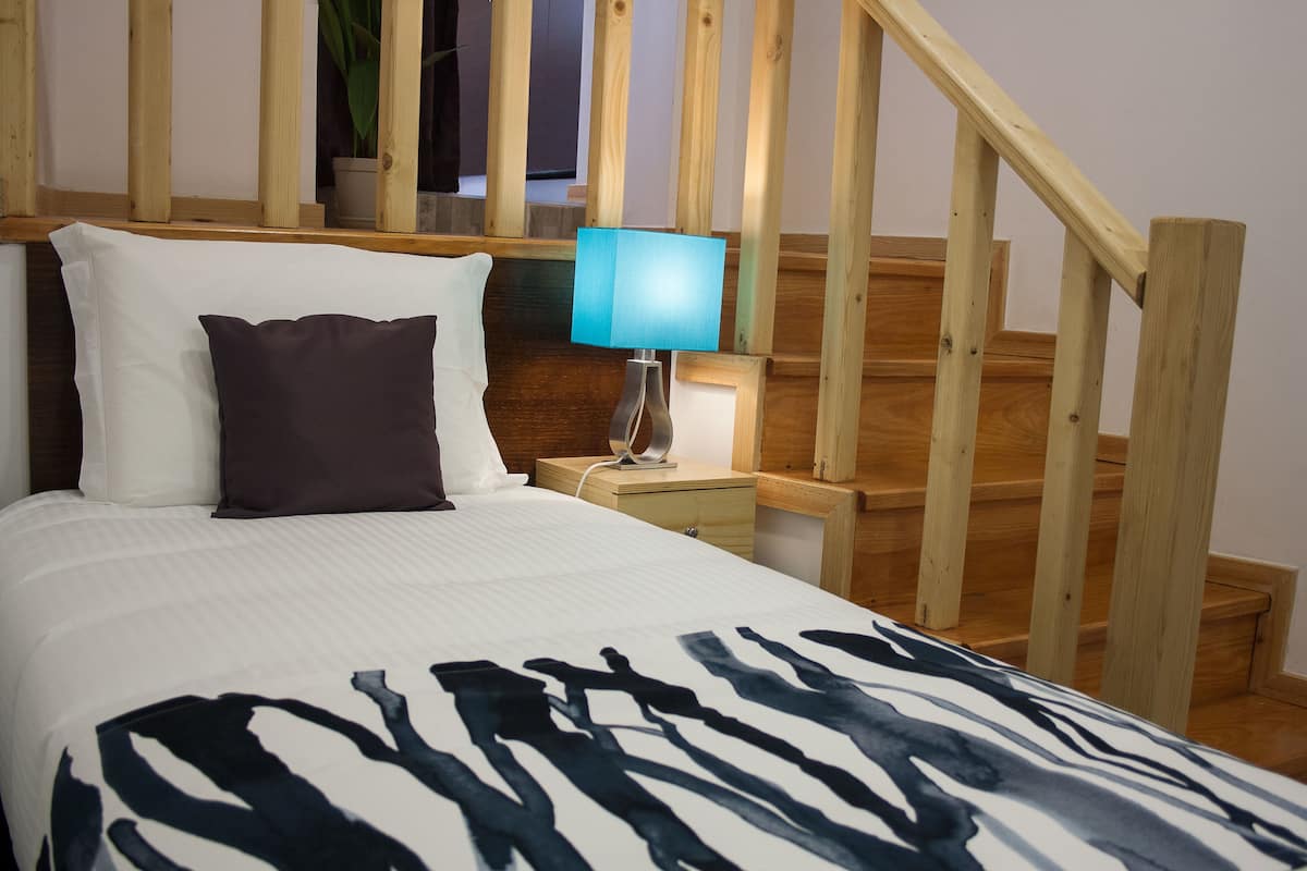 Una habitación de hotel con una cama, una mesita de noche, una lámpara y una escalera de madera.