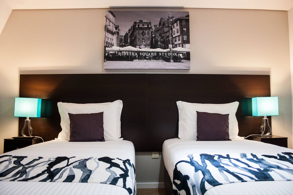 Una habitación de hotel con dos camas, un cabecero oscuro y un cuadro enmarcado encima de las camas.