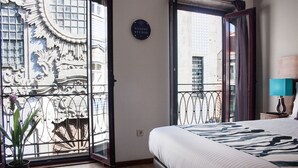 Habitación de hotel con cama, planta en maceta, ventana con reja decorativa y un cartel en la pared.