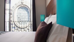Habitación de hotel con una cama grande, vistas a la fachada de un edificio y una ventana con celosía decorativa.