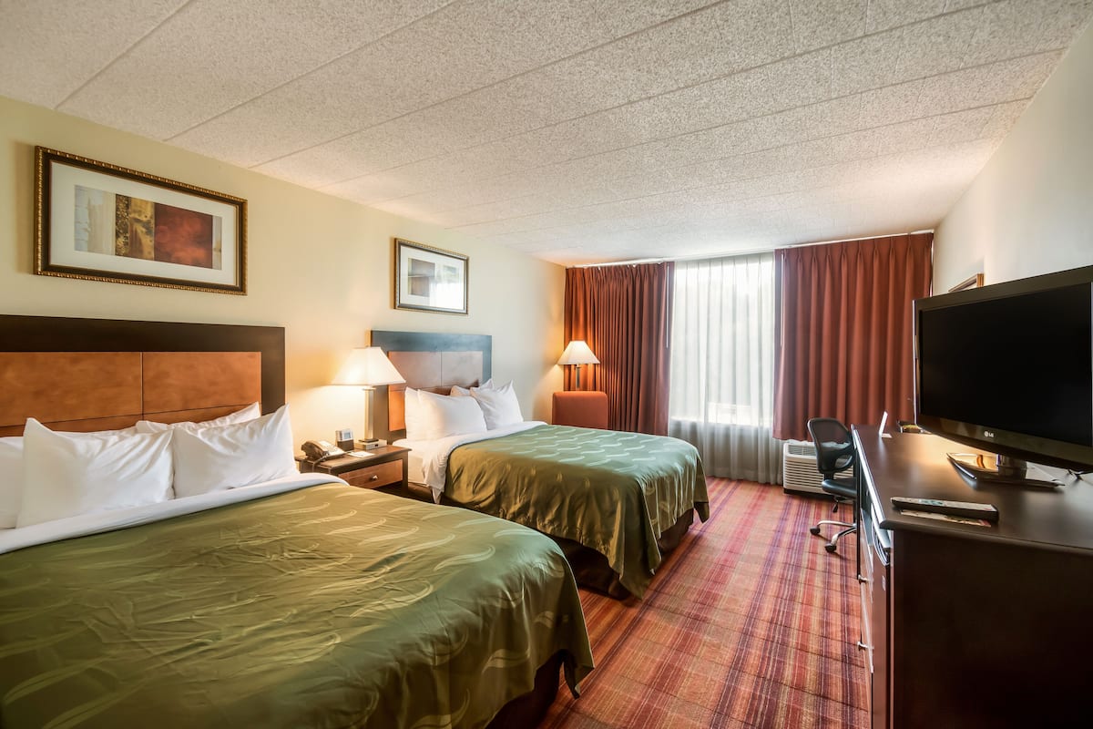A hotel room with two beds, a desk, a television, and a window with curtains.