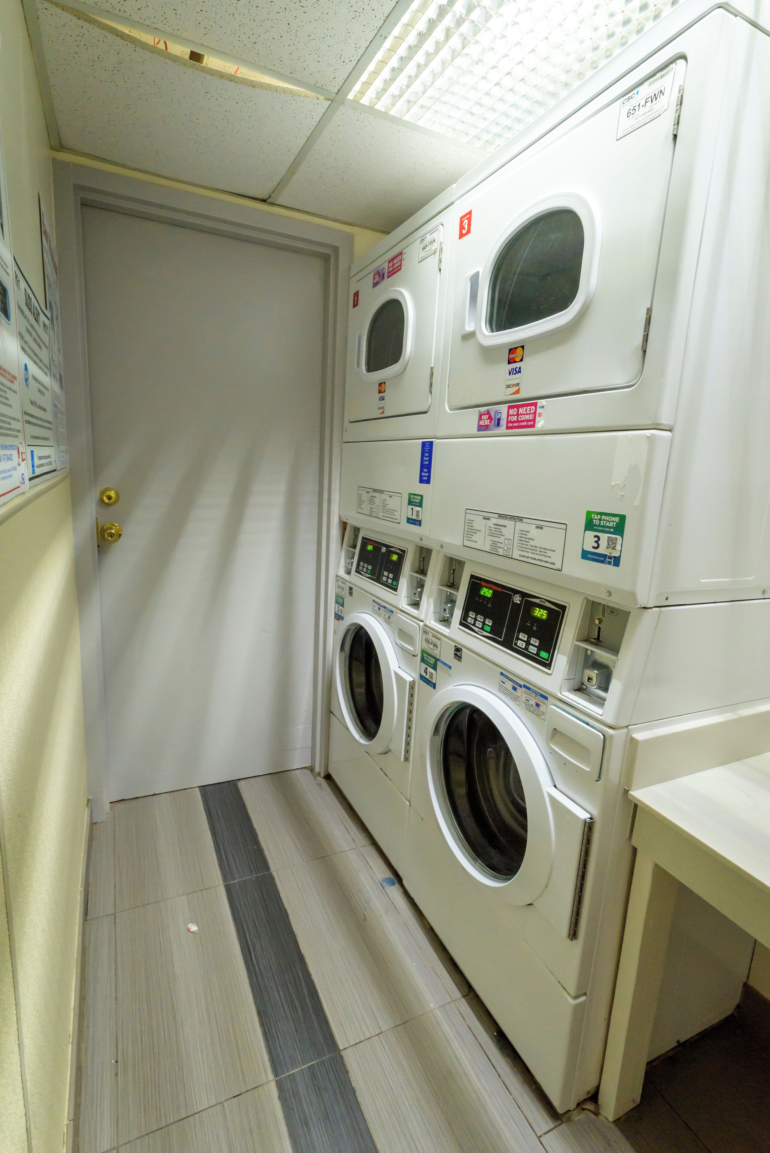 A laundry room with stacked washers and dryers, a door, and a tiled floor.