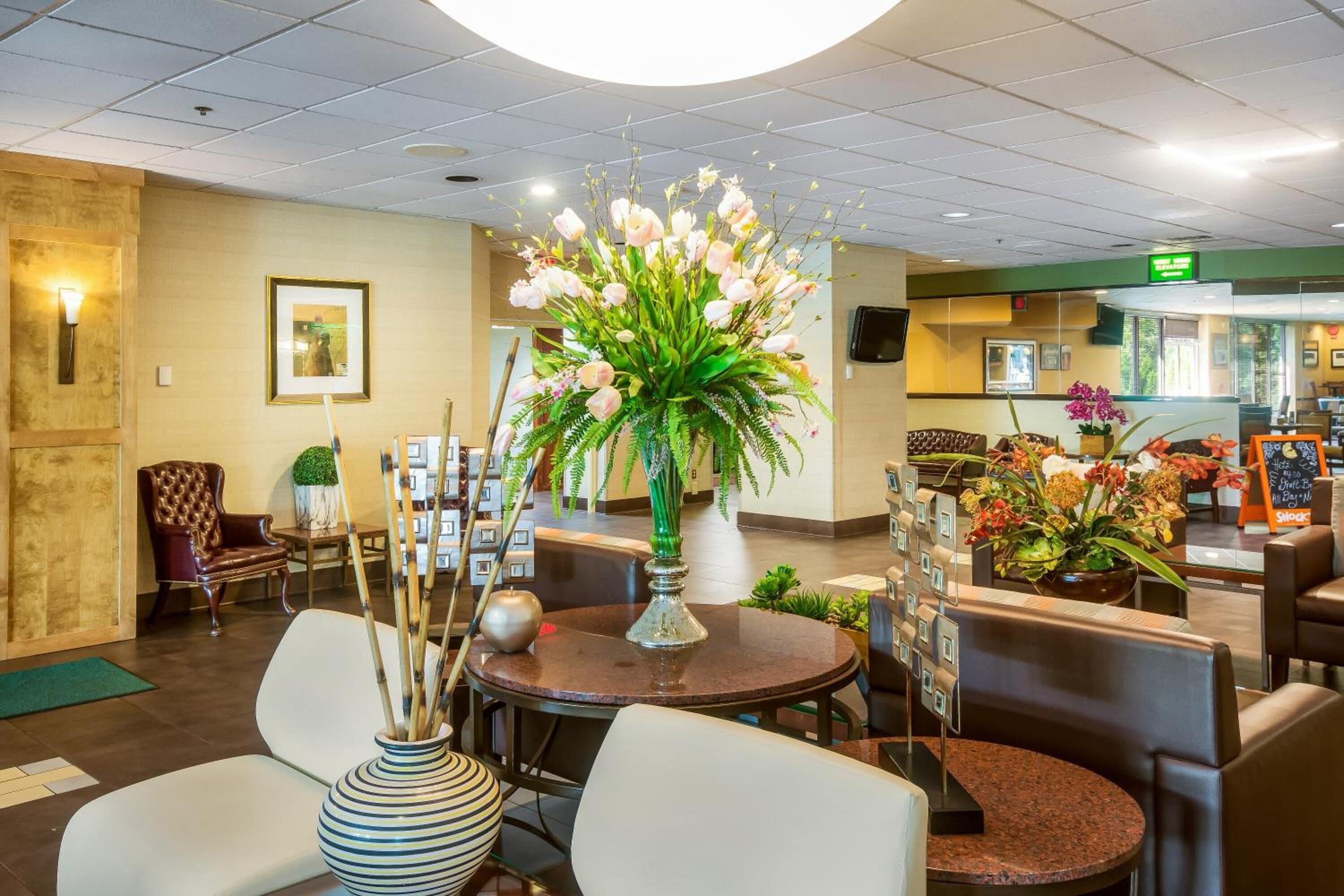 A hotel lobby with a reception desk, seating area, and a large floral arrangement.