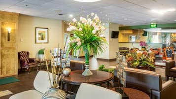 A hotel lobby with a reception desk, seating area, and a large floral arrangement.